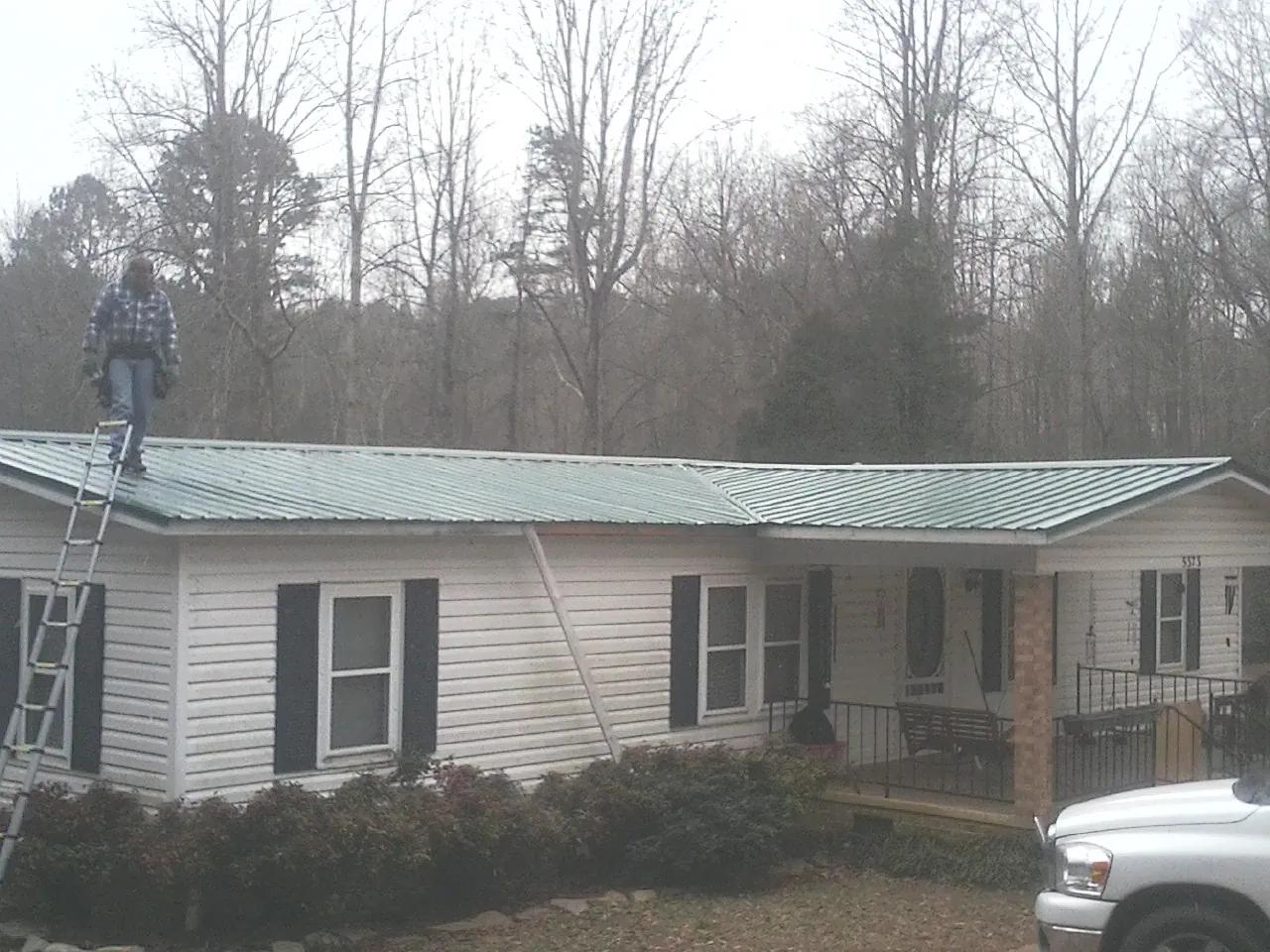 Worker on a ladder beside a new green metal roof on a ranch home in Princeton